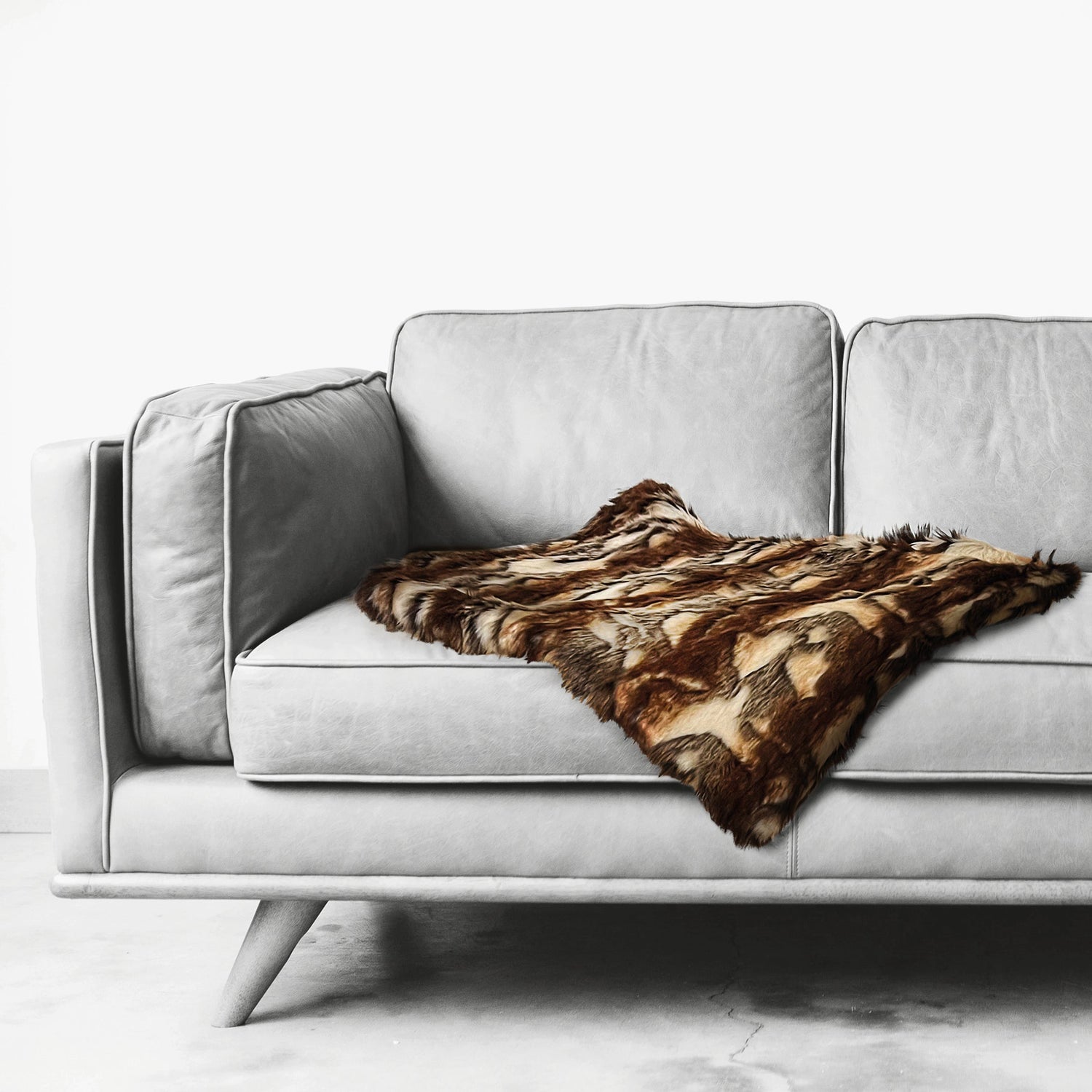 Langhaarkunstfelldecke für Hunde in dunkelbraun & beige gemustert liegt auf einer grauen Couch 